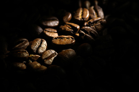 Coffee beans background. 
Brown texture of roasted coffee seeds filling all frame. 
Space for copy text.
Selective spot light, back light, shallow depth of field, selective focus. Extreme close up.の写真素材