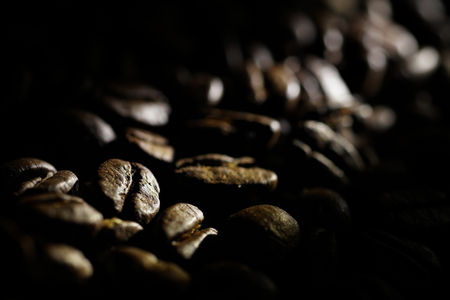 Coffee beans background. Brown texture of roasted coffee seeds filling all frame. Space for copy text.Selective spot light, back light, shallow depth of field, selective focus. Extreme close up.の写真素材