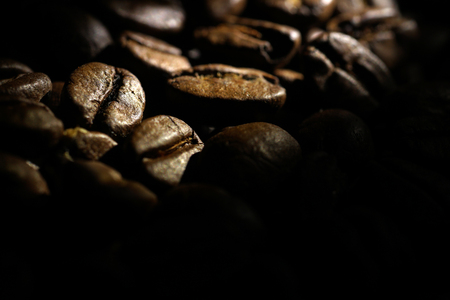 Coffee beans background. 
Brown texture of roasted coffee seeds filling all frame. 
Space for copy text.
Selective spot light, back light, shallow depth of field, selective focus. Extreme close up.の写真素材
