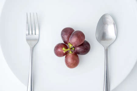 health eating of fruit, red grape on white plate with fork and spoonの写真素材