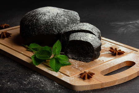fresh black rye bread on a cutting board with seasonings sprinkled with flour on a black wooden tableの写真素材