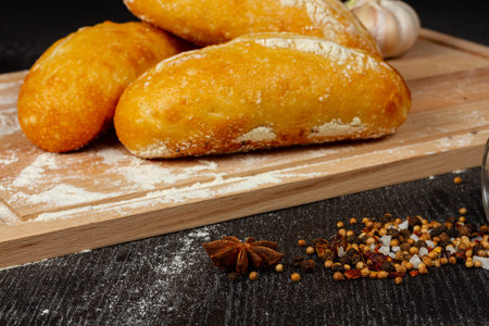fresh wheat white bread on a cutting board with seasonings sprinkled with flour on a black wooden...