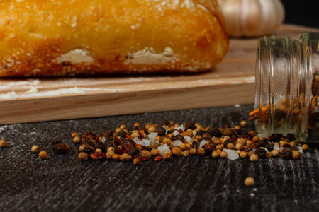 fresh wheat white bread on a cutting board with seasonings sprinkled with flour on a black wooden tableの写真素材