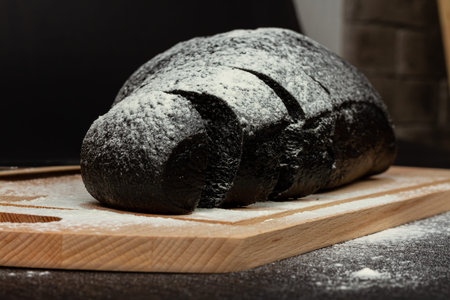 fresh fragrant black rye bread on a cutting board with flour on a black wooden table