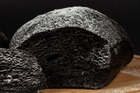 fresh fragrant black rye bread on a cutting board with flour on a black wooden tableの写真素材