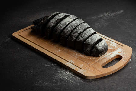 fresh black rye bread on a cutting board with seasonings sprinkled with flour on a black wooden tableの写真素材