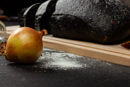fresh black rye bread on a cutting board with seasonings sprinkled with flour on a black wooden...