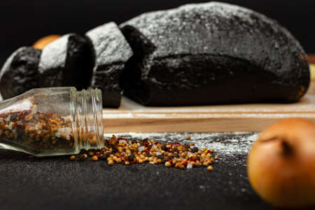 fresh black rye bread on a cutting board with seasonings sprinkled with flour on a black wooden tableの写真素材
