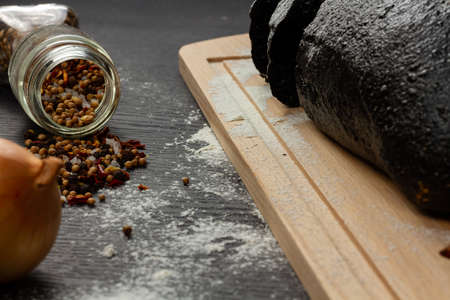 fresh black rye bread on a cutting board with seasonings sprinkled with flour on a black wooden tableの写真素材