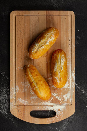 fresh wheat white buns on a cutting board with flour on a black wooden tableの写真素材