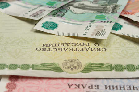 birth certificate and paper money lie on a white wooden table inscription birth and marriage certificateの写真素材