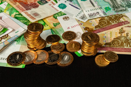 stack of metallic gold coins and paper money lie on a black wooden table