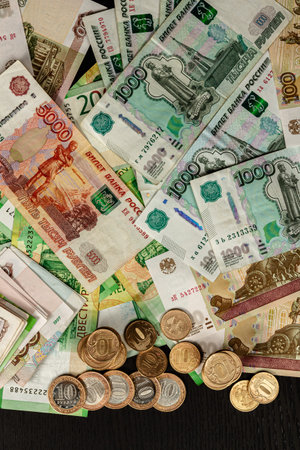 a lot of Russian metal coins and paper money lie on a black wooden table