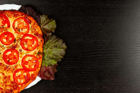 delicious fragrant pizza with herbs in a white plate on a wooden black tableの写真素材