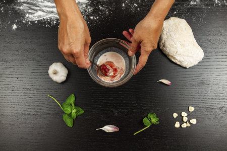 chef girl stirring tomato paste with cream, garlic and seasonings to make fresh italian homemade...