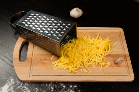 grated fresh aromatic cheese for pizza, garlic and grater lie on a wooden kitchen boardの写真素材
