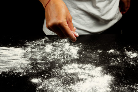 girl chef sprinkles flour on black wooden kitchen table to make homemade dough
