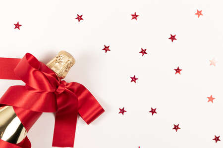 a gift bottle of champagne in golden foil wrapped in a red silk ribbon and scattered confetti on a white backgroundの写真素材
