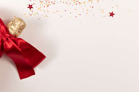 a gift bottle of champagne in golden foil wrapped in a red silk ribbon and scattered confetti on a white backgroundの写真素材