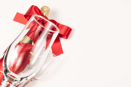 empty wine glass in the foreground against the background of a bottle of champagne wrapped with a red silk ribbon on a white backgroundの写真素材