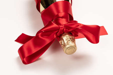 gift bottle of champagne in gold foil wrapped with red silk ribbon bow on white backgroundの写真素材