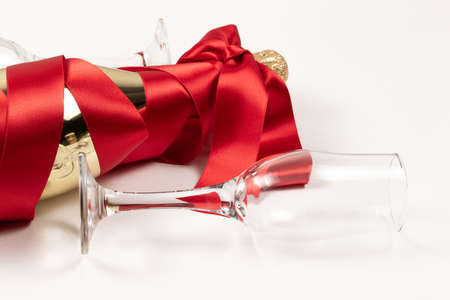 gift bottle of champagne in gold foil wrapped in a red silk ribbon and two glasses on a white backgroundの写真素材