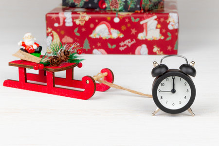 santa claus on a sleigh, boxes with gifts and an alarm clock on a white wood background