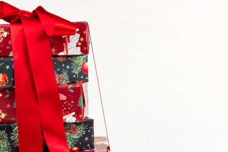 festive multicolored Christmas boxes tied with a red satin ribbon with gifts stacked on a white wooden tableの写真素材