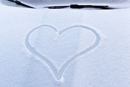 image of a heart in the snow on the hood of a car on a bright frosty winter dayの写真素材