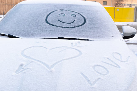 image of a smiling face in the snow on the windshield of a car and a heart shape on a frosty winter dayの写真素材