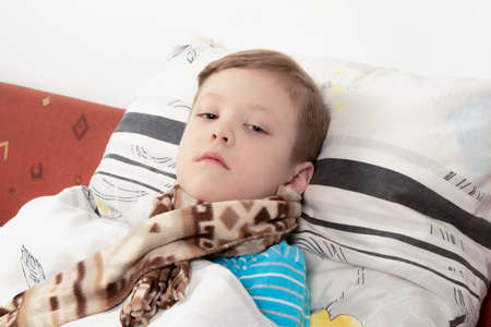 sick child boy in a blue sweater with a scarf in bed waiting for recoveryの写真素材