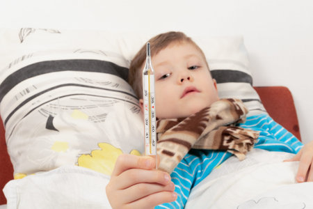 a sick child a boy in a blue jacket lies at home in bed and measures the temperature with a...