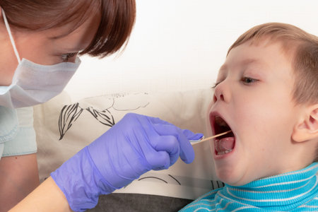 girl doctor in blue medical gloves and a mask examining the throat of a sick child boy