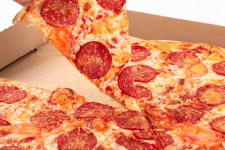 a female hand holds a piece of fresh fragrant pizza, the rest of the pizza lies in the box. close-upの写真素材