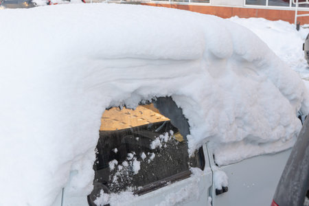 old white abandoned broken rusty car parked by the road under a large layer of snow on a cold winter...