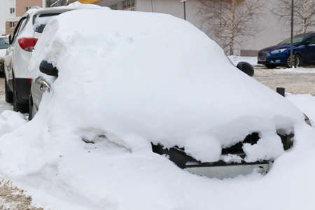 old abandoned broken car parked by the road under a large layer of snow on a cold winter dayの写真素材