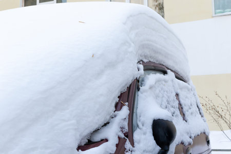 red abandoned car in winter parked under a large layer of snow on a bright sunny frosty day