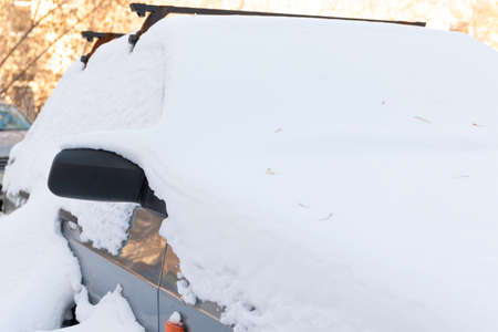old abandoned broken car parked by the road under a large layer of snow on a cold winter dayの写真素材
