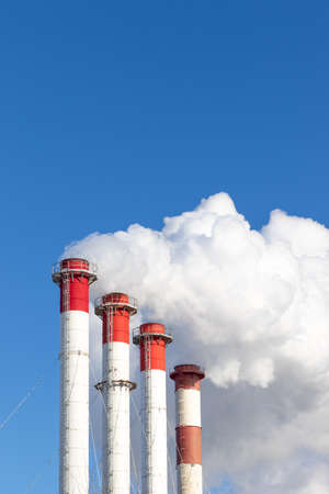 red-white chimneys of the boiler room, equipped with a traffic light. white smoke against blue sky on sunny frosty winter dayの写真素材