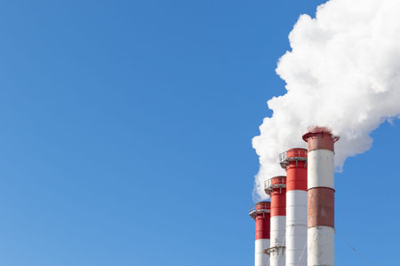 red-white chimneys of the boiler room, equipped with a traffic light. white smoke against blue sky...