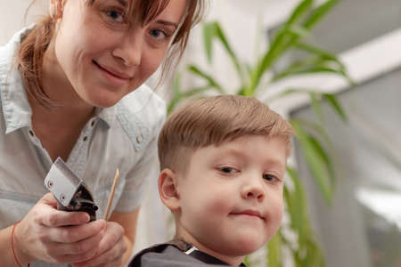 young mom hairdresser cuts her baby boy at home with hair clipper during quarantine. selective focus. portraitの写真素材