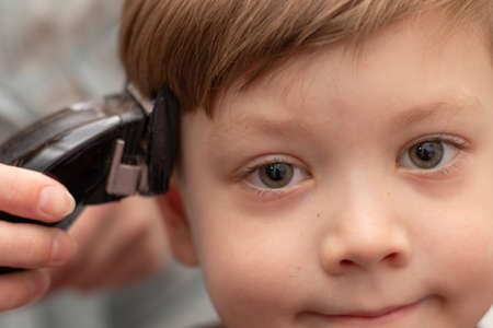 close-up portrait of a cute preschooler boy whose female hands are cut with a hair clipper. look into the camera. selective focusの写真素材