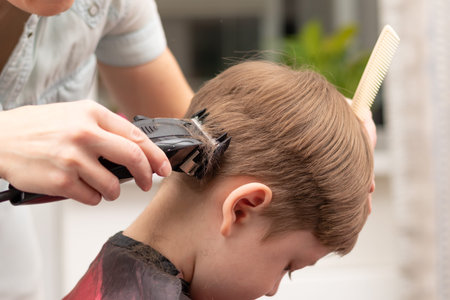 young mom hairdresser cuts her baby boy at home with hair clipper during quarantine. selective...