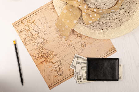 world map, straw hat, black leather wallet with money and a pencil on a white wooden table. view from aboveの写真素材