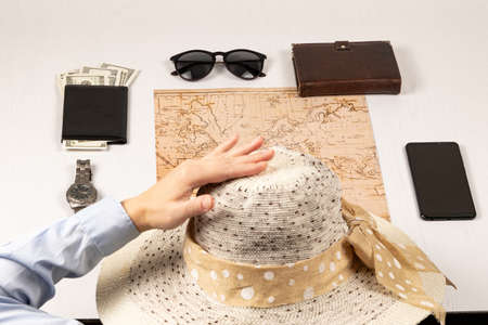 female hand holds a straw hat. on a white wooden table lies a world map, a black wallet with money, a diary, a watch, a smartphone and sunglasses. selective focusの写真素材