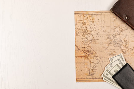 world map, black leather wallet with money and brown leather diary on a white wooden table. view...