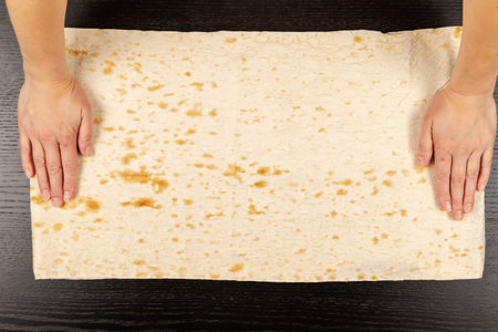 female hands lay out fresh pita bread for making shawarma on the background of a black wooden table...