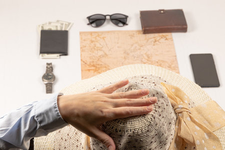 female hand holds a straw hat. on a white wooden table lies a world map, a black wallet with money, a diary, a watch, a smartphone and sunglasses. selective focusの写真素材
