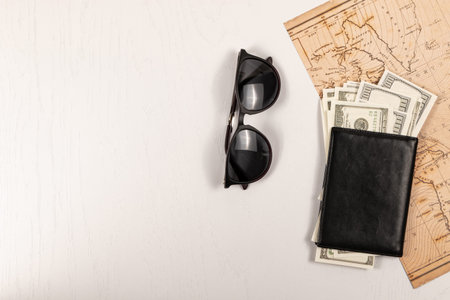 world map, black leather wallet with money and sunglasses on a white wooden table. view from above....