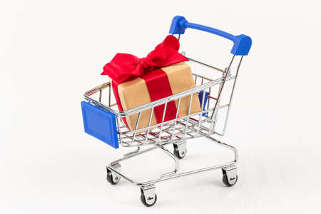 gift box with a red bow and ribbon in a metal shiny shopping trolley on wheels on a white background. close-upの写真素材